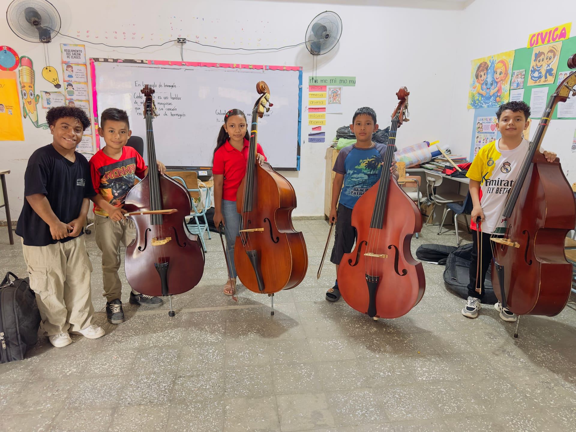 Cinco niñas y niños sonríen junto a sus contrabajos en un aula
