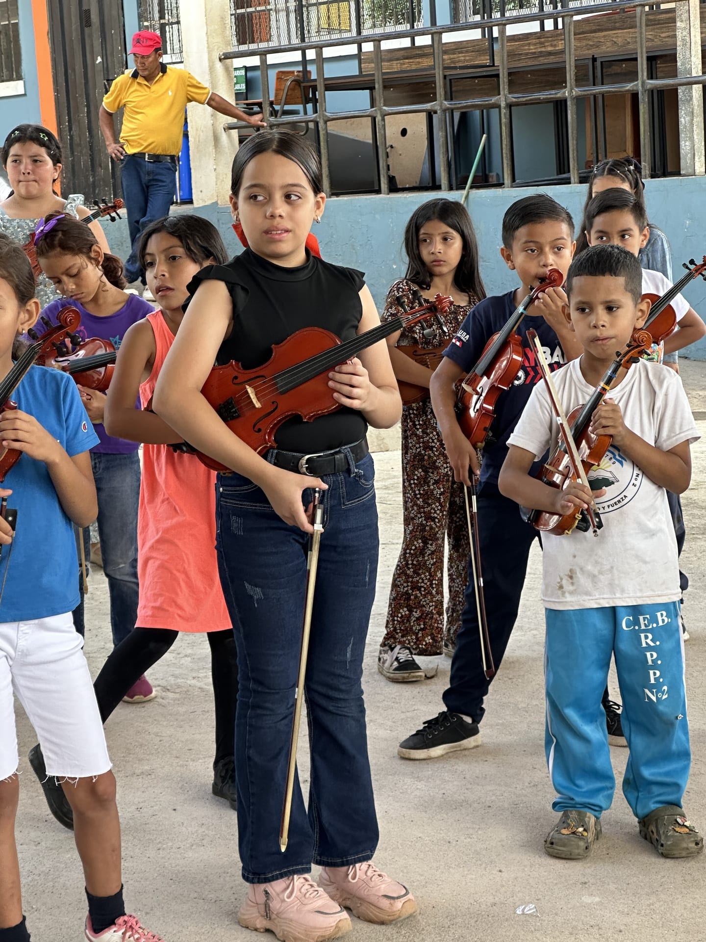 Niñas y niños con sus violines y arcos, atentos a la clase en el patio de la escuela