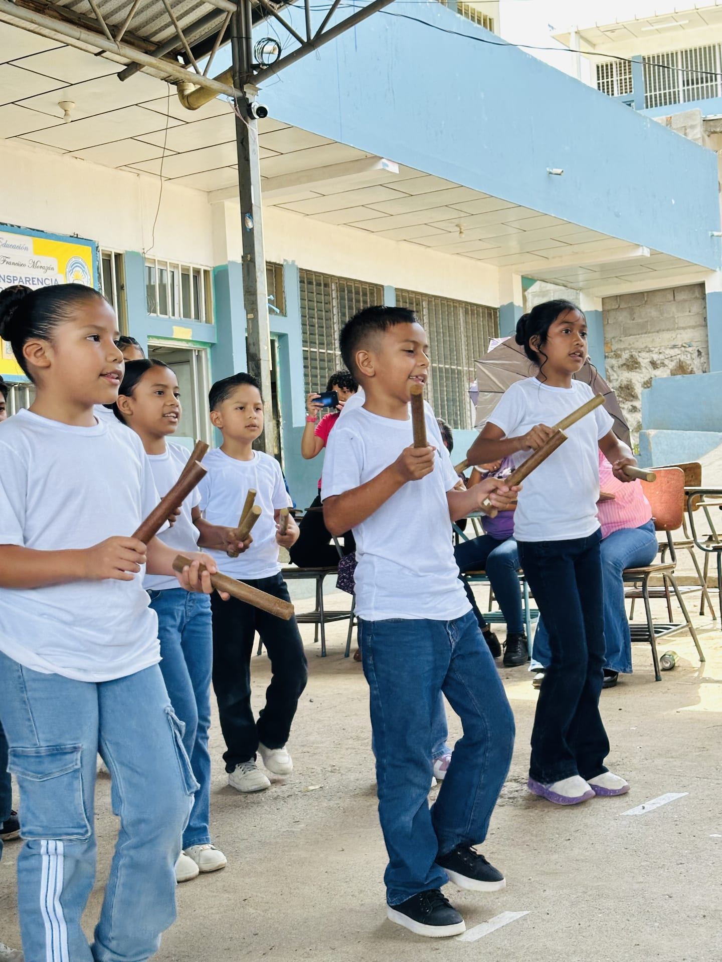 Niñas y niños marcan el ritmo con palitos de madera, al aire libre