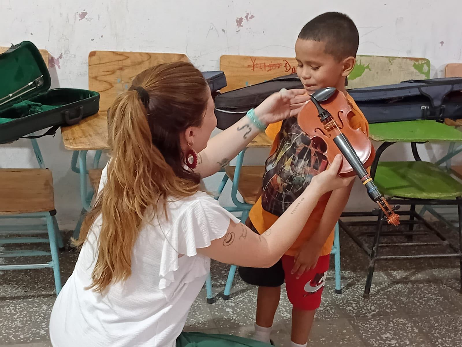 Una persona adulta ayuda a un niño a colocar correctamente el violín durante una clase